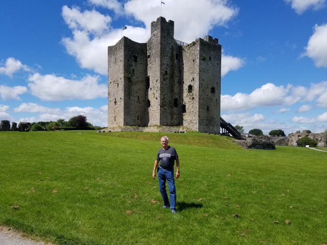 Image of Prof. Robert Cooney of the University of Hawaii Manoa Office of Public Health Studies, Summer in Dublin, Ireland, faculty resident director, posing in front of Trim Castle, built by his 26th great-grandfather Hugh De Lacy around 1200 AD and used for the filming of the movie “Braveheart”.